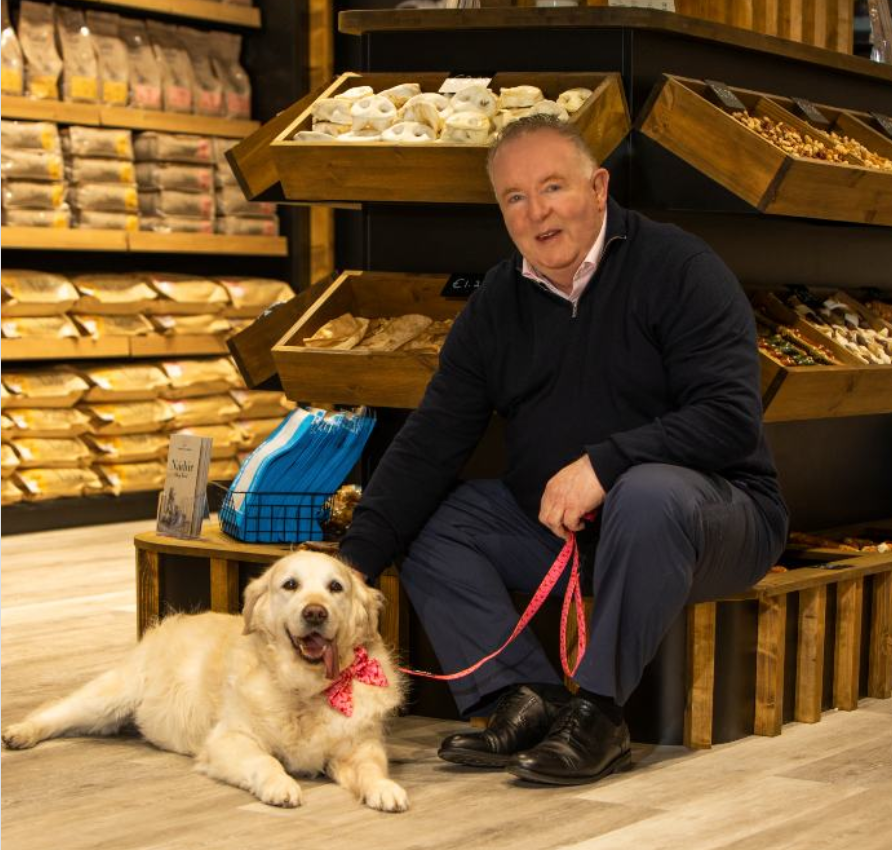 Anthony Gallagher, Owner and Managing Director of Petstop, sitting in-store with a golden retriever wearing a red bow at his feet