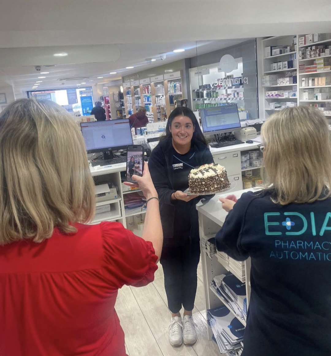A Reens team member behind the dispensary counter holding a celebration cake, being filmed for the team's social media