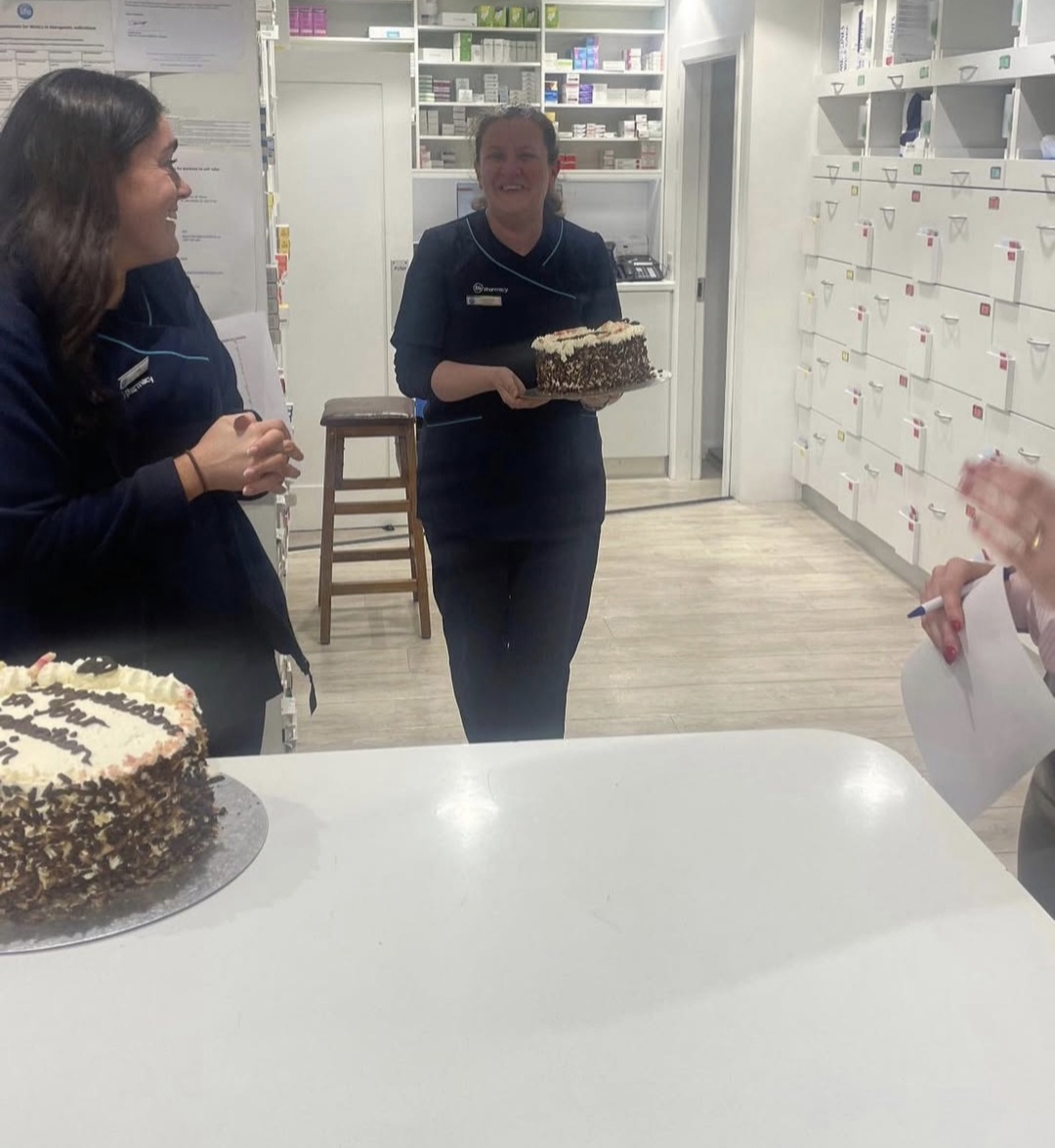 A Reens Life Pharmacy team member presenting a celebration cake on a stool