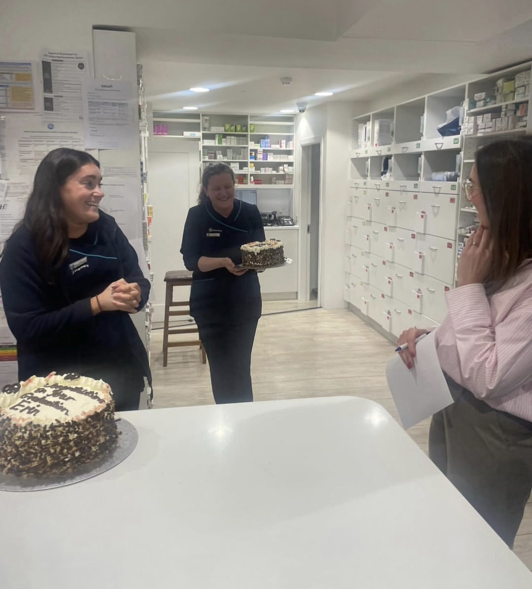 Two members of the Reens team laughing as a colleague brings out a celebration cake