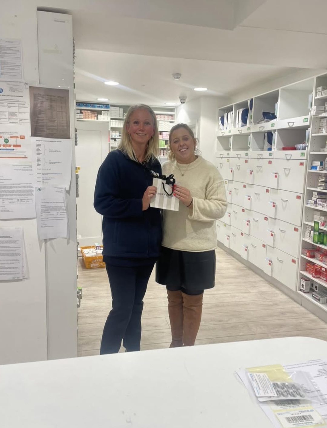 Louise Lally and Mairead Reen standing together in the Reens dispensary holding a small gift bag